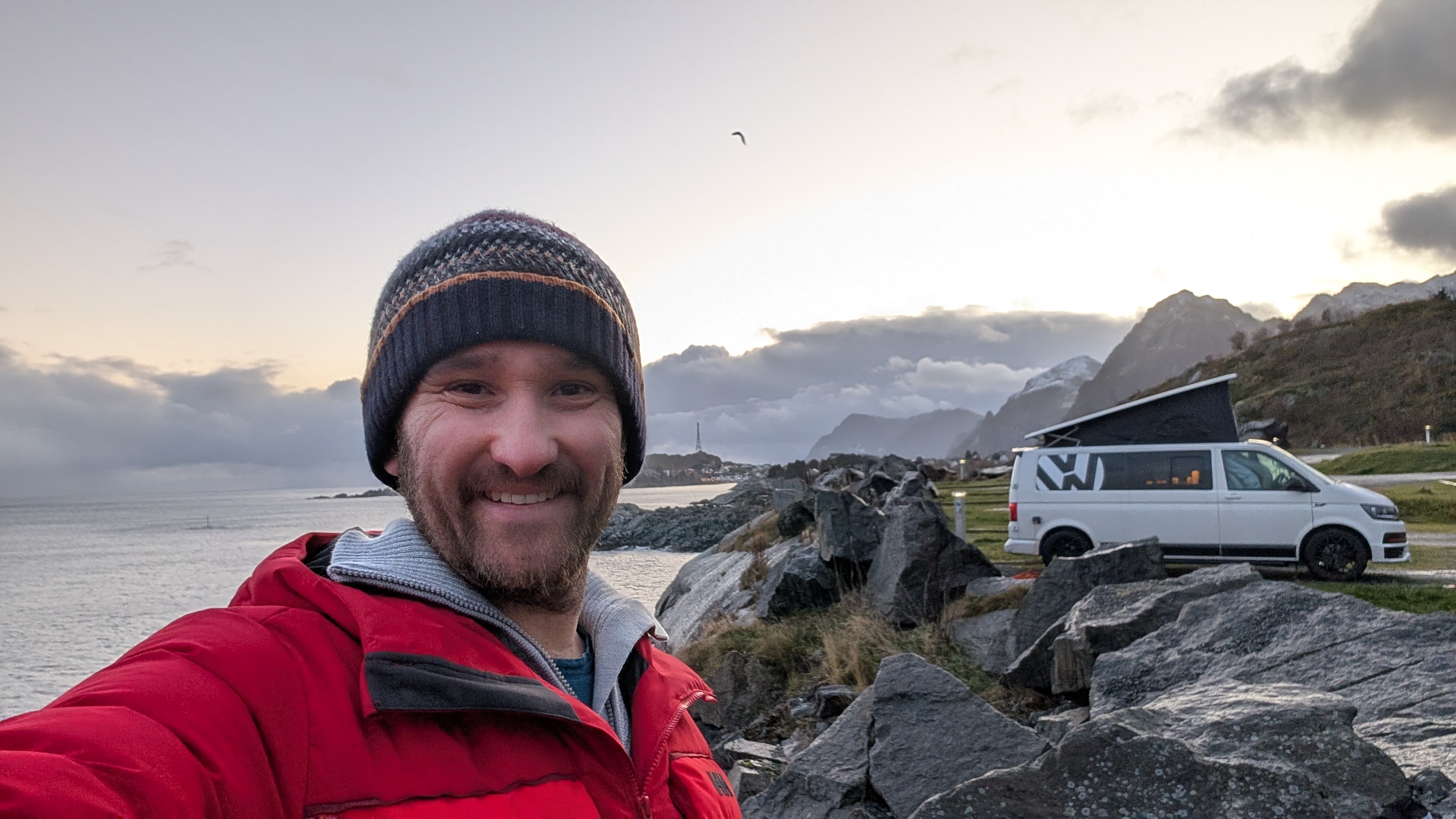 A picture showing a relieved bearded man in a red coat. Sunny morning in northern Norway after a hectic few days sheltering from the worst of autumn storms in a campervan.
